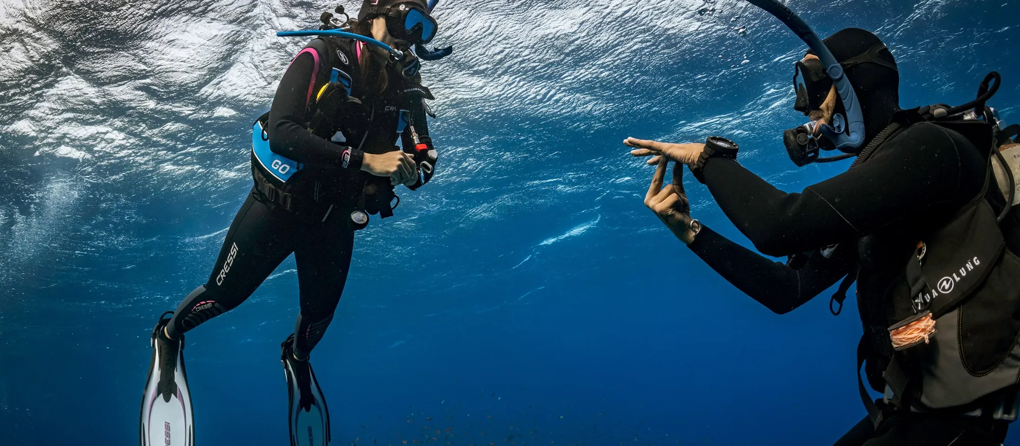 An instructor guiding a student with a calm hand signal just below the surface